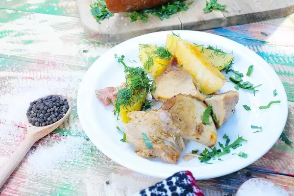 Schweinebraten mit Kartoffelecken auf einem weißen Teller. Salz und Pfeffer auf einem bunten Tisch im Vintage-Stil