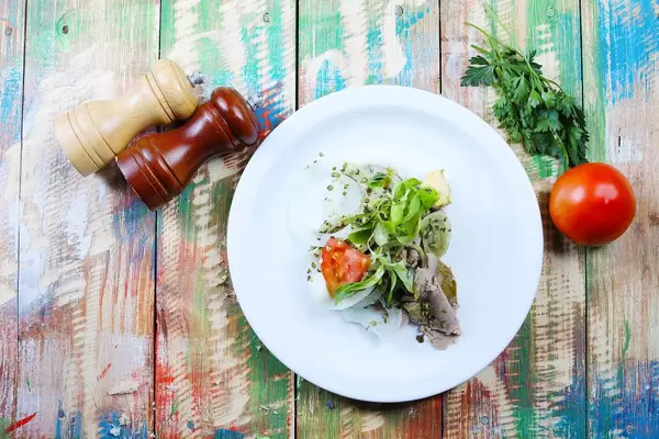 Schweinefleisch mit frischer Tomate auf einem weißen Teller vor hölzernem Hintergrund im Vintage-Stil