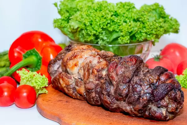 Schweineroulade mit Gemüse wie Tomaten und Paprika auf Küchenbrett mit Kraussalat