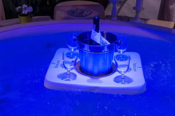 Schwimmende Insel mit Champagnerkühler und vier Gläsern in Whirlpool in blauem Licht