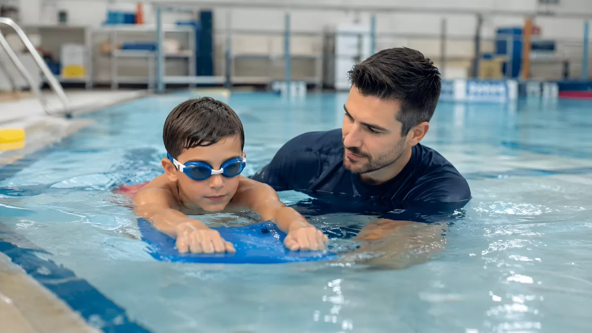 Schwimmtrainer zeigt Kind Technik mit Kickboard