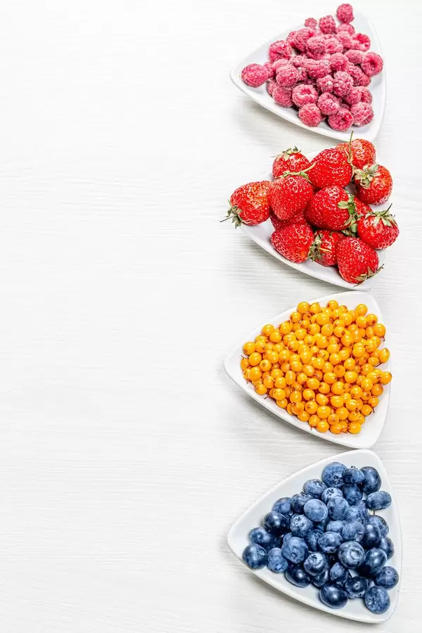 Sea buckthorn, blueberries, raspberries and strawberries on white wooden background