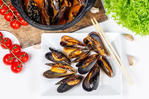 Sea food, delicious mussels with spicy sauce on a white background with vegetables, top view