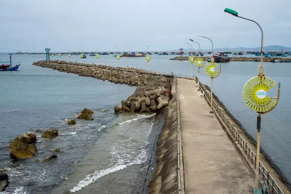 Sea Walkway with Street Lights and Tetrapod Structures at Phu Quoc Harbour with Fishing Boats and Mountains in the Background in Vietnam