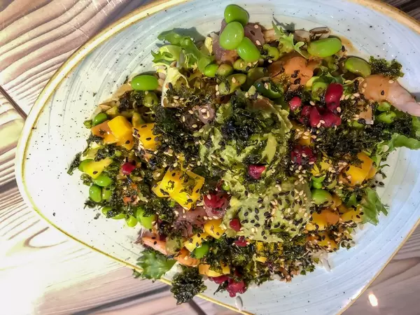 Seafood salad with rice, mango, beans and seed topping on white-blue plate from close perspective