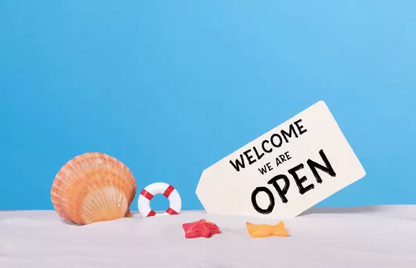 Seashells with Welcome we are open sign on sandy beach