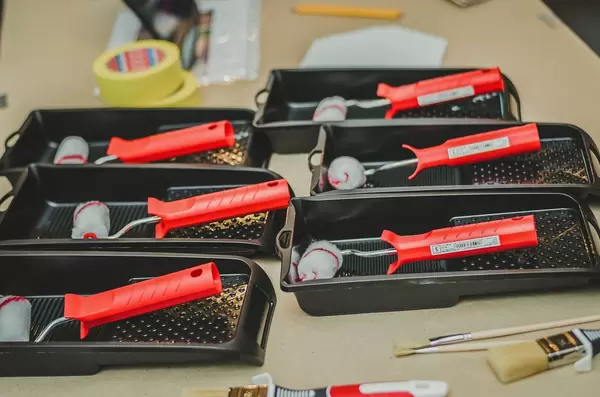 Sechs Farbroller mit kleiner Stoffrolle in Farbschale vor weiteren Malerutensilien