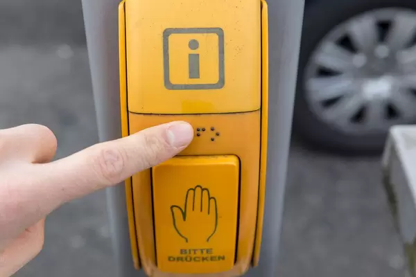 Sehbehinderter Fußgänger liest Blindenschrift an gelbem Druckknopf für Ampelanlage in Köln