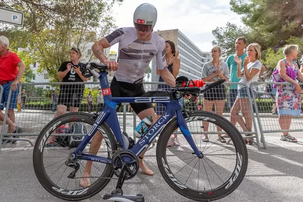 Seitenansicht eines Athleten mit der Nummer 23 beim Challenge Triathlon der sich auf ein blaues Rennrad aufsetzt