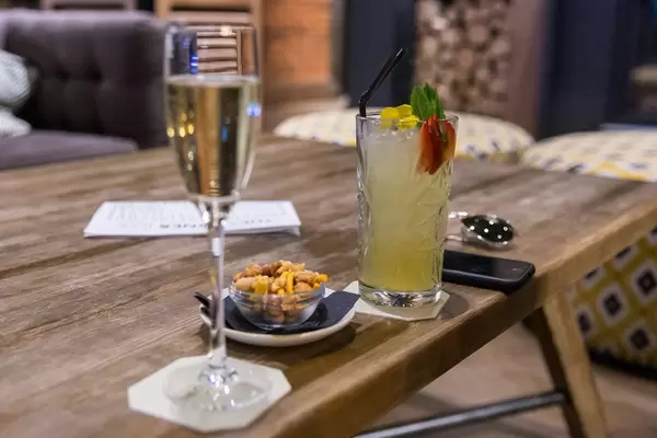 Sekt,Cocktail, Handy und kleine Schale Nüsse auf einem rustikalen Holztisch in der Lounge und Bar des The Corner Hotels in Barcelona, Spanien