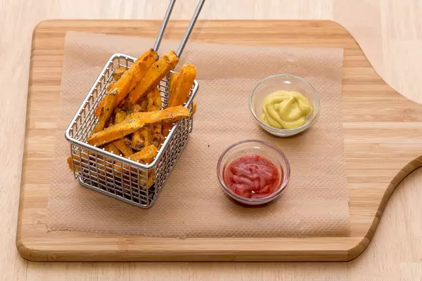 Selbstgemachte Süßkartoffel-Pommes mit Ketchup und Senf in Servier-Friteuse