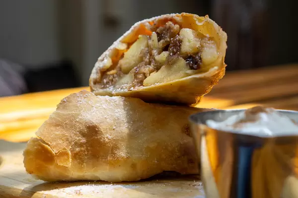 Selbstgemachter Apfelstrudel mit Rosinen, frischen Äpfeln und Puderzucker auf einem Holzbrett mit Schlagsahne und Zimt Nahaufnahme