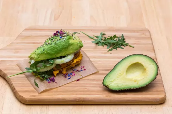 Selbstgemachter Avocado-Burger mit Sesam, Kräutern, Zwiebeln, Humus und Veggie-Frikadelle