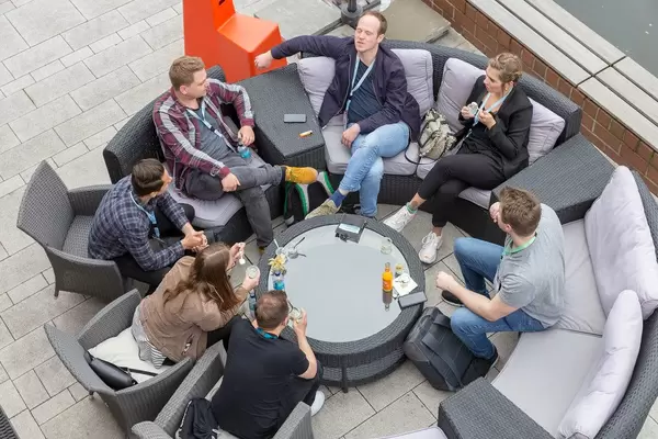 Selbstständige und Teilnehmer des Barcamp OMWest19 von AXA in Köln, machen eine Pause auf runden Rattanmöbeln auf einer Terasse