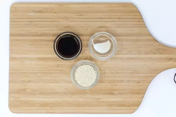 Sesam, Sojasauce und Knblauchzehe in Schälchen auf Brett  - Aufsicht