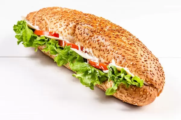 Sesambrot-Sandwich mit Salat, Tomaten, Schinken und Käse auf weißem Tisch