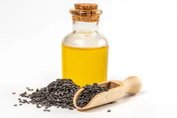 Sesame oil in glass bottle with black sesame seed in wooden scoop on white