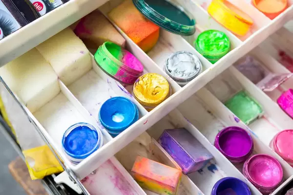 Set aus Theaterschminke mit Schwämmen und Farbtöpfen in blau, gelb, grün und pink in weißer Plastikbox