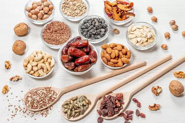 Set nuts, seeds, dried fruits in different bowls and wooden spoons on white wooden background (Flip 2019)