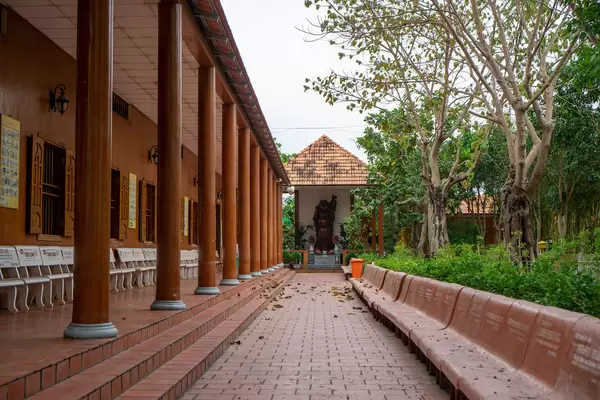 Several Stone Benches next to a Buddhist Building with Red Pillars leading to a Buddha Statue at Truc Lam Phuong Nam Zen Monastery in Can Tho, Vietnam