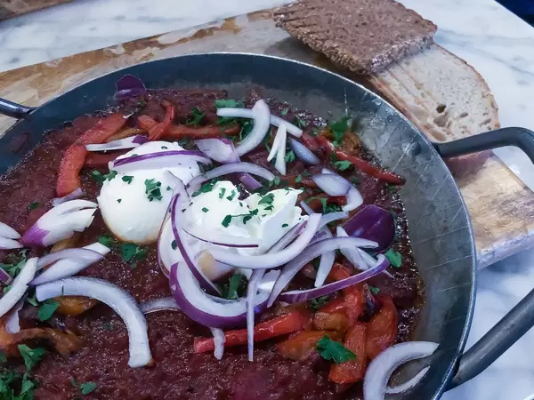 Shakshuka: a steaming hot North African casserole with tomatoes, fresh peppers, red onions, two eggs and toasted bread