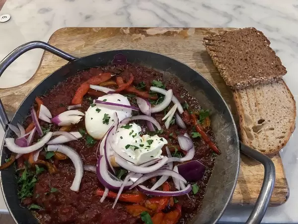 Shakshuka: eine dampfend heisse, Nordafrikanische Schmorpfanne mit Tomaten, frischer Paprika, roten Zwiebeln, zwei Eiern und geröstetem Brot