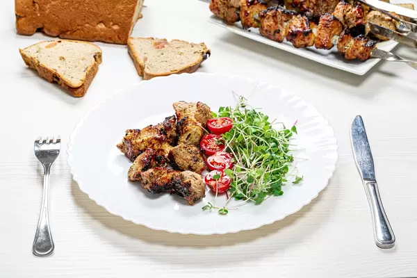 Shashlik with micro greens radish and tomato slices on a white wooden table with a knife and fork