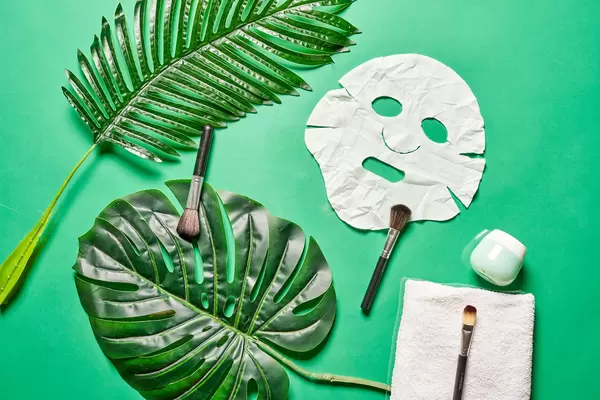 Sheet facial mask with cosmetic products on green background