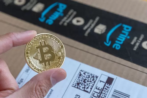 Shopping with Bitcoin on Amazon is no more a fiction - Hand shows gold-colored coin with big Bitcoin logo in the middle