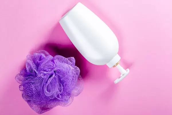 Shower gel and purple washcloth on pink background