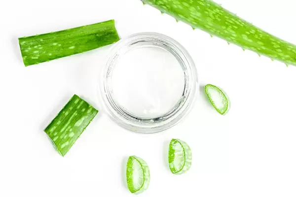 Sicht von oben auf Aloe Vera Gel in einem Glas, neben grünen Blättern, vor weißem Hintergrund