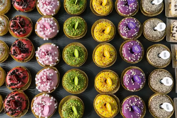 Sicht von oben auf Dots original Rainbow-Donuts mit Pistazien, Yellow Frutti, Marshmallow und Red Cookie