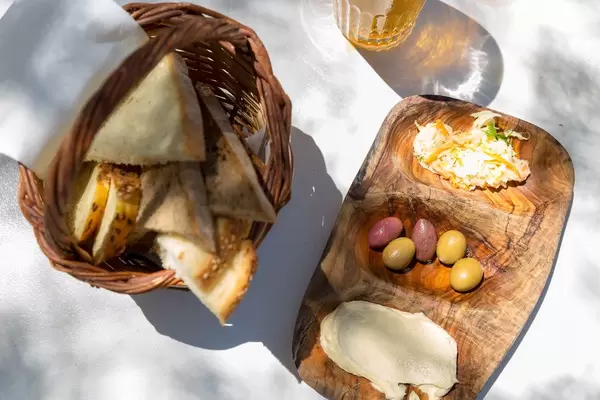 Sicht von oben, auf ein Korb mit verschiedenen Brotscheiben, mehrfarbigen Oliven und Hummus, auf einem Holzbrettchen