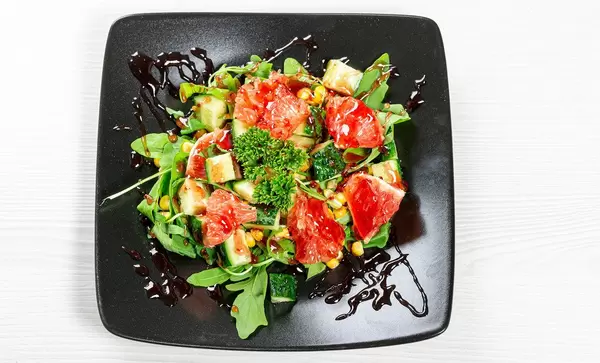 Sicht von oben auf einen gesunden Salat mit Rucola, buntem Gemüse und roten Grapefruitscheiben, auf einem schwarzen Teller