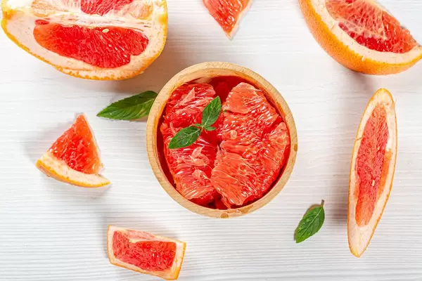 Sicht von oben auf geschnittene Grapefruitscheiben und Fruchtstücke, auf einer weißen Oberfläche