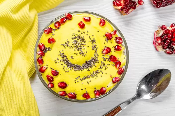 Sicht von oben auf Haferflocken mit Granatapfel und Chiasamen, neben einem Löffel und gelbem Küchentuch