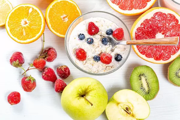 Sicht von oben auf Haferflocken zum Frühstück, mit reifen Beeren, gesundem Obst und halbierten Früchten, auf einem Holztisch