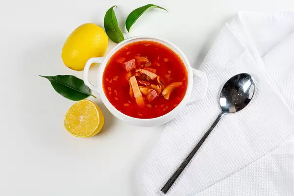 Sicht von oben auf Soljanka-Suppe mit geräuchertem Hühnchen, Kalbsfleisch und Schinken, mit Zitronen auf einem weißen Tisch