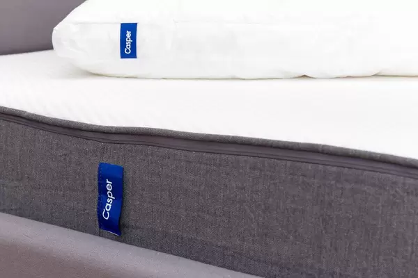 Side view of the breathable and ergnomic Casper mattress in white and grey with Casper pillow