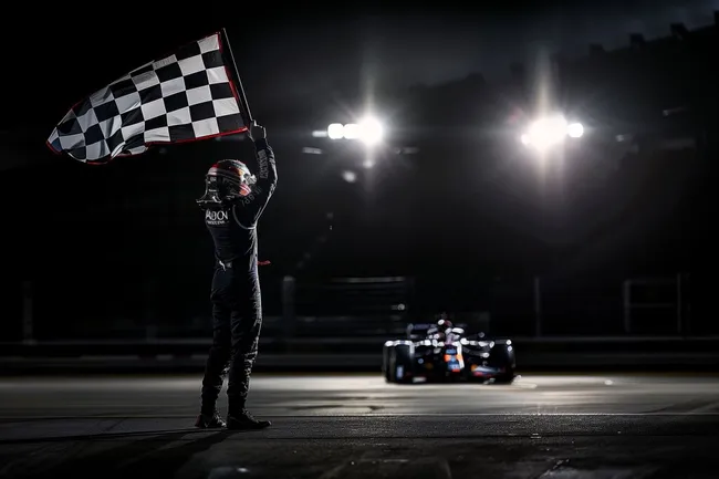 Siegesfeier mit Zielflagge und Formel 1 Auto bei Nacht