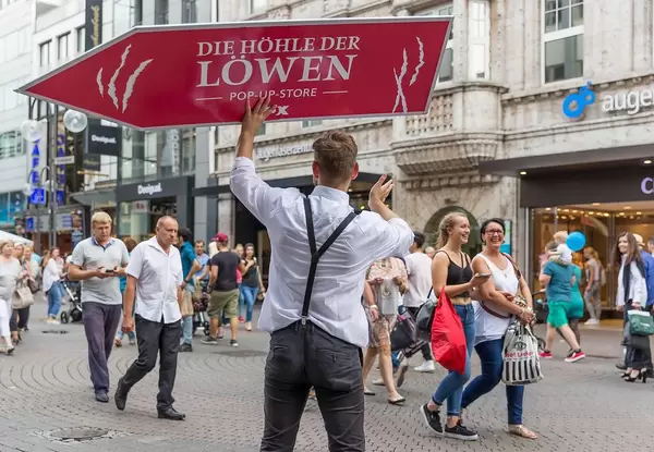 Sign spinning with "Die Höhle der Löwen Pop up store" in a German shopping street