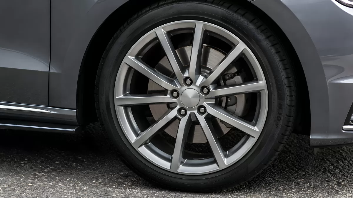 Silberne Alufelge mit Bremsscheibe an grauem Auto