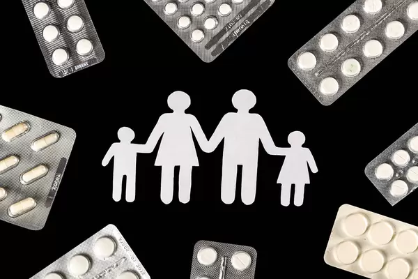 Silhouette of a family on a black background with a frame of pills in blisters, top view