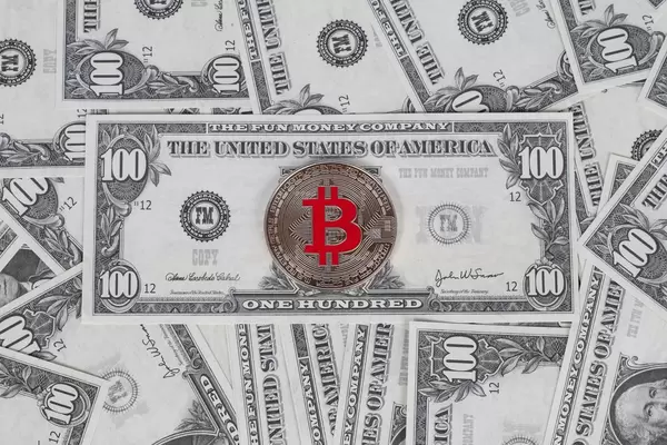 Silver coin of Bitcoin cryptocurrency on 100 USD banknote