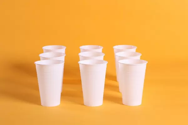Single use white plastic cups on a orange background