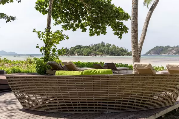 Sitzecke mit Rattanmöbel zum Entspannen unter Palmen mit Blick auf den indischen Ozean und Strand von Mahé auf den Seychellen-Inseln