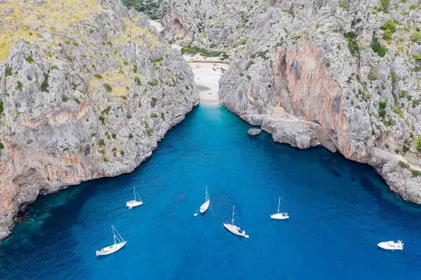 Six boats in the blue waters by the entrance of the bay of Sa Calobra. Bird's eye view in Mallorca