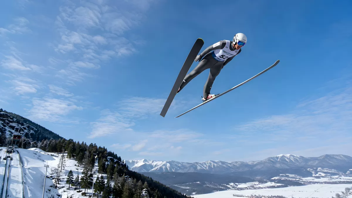 Skispringer fliegt über verschneite Alpenlandschaft