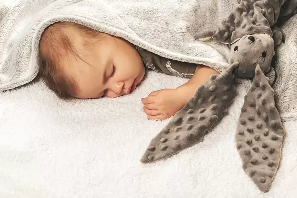 Sleeping baby on the bed covered with a blanket with a toy rabbit