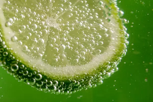 Slice of fresh lime with bubbles on green background